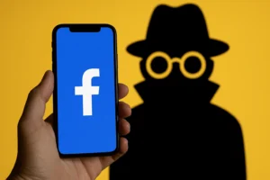 Mão segurando celular com o logo do Facebook em destaque, enquanto uma silhueta misteriosa aparece ao fundo, representando quem espiona seu perfil.